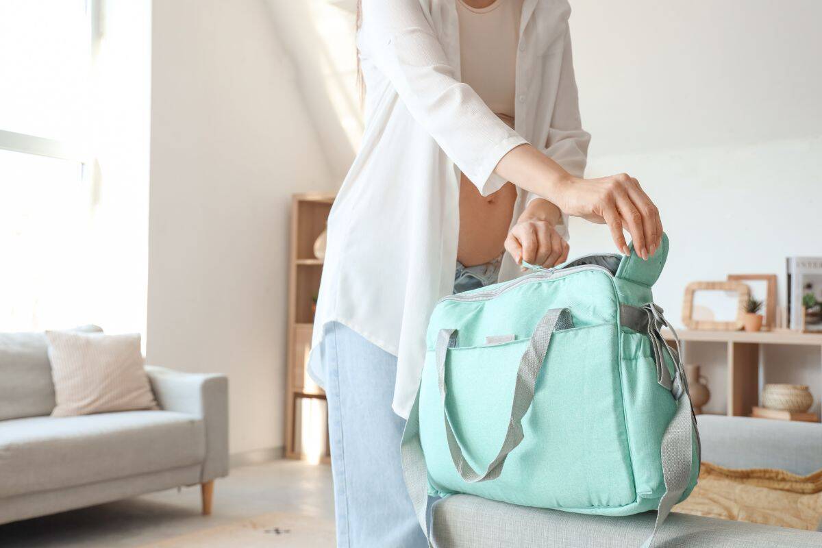 Pregnant woman packing a mint green hospital bag at home, preparing essentials for labor and delivery.