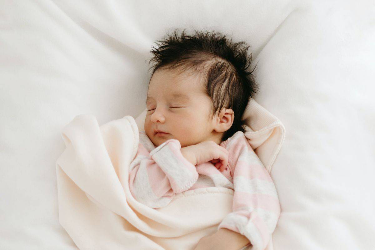 Newborn baby girl peacefully sleeping in a soft pink blanket — a sweet moment capturing the gentle charm that inspires beautiful three syllable girl names.
